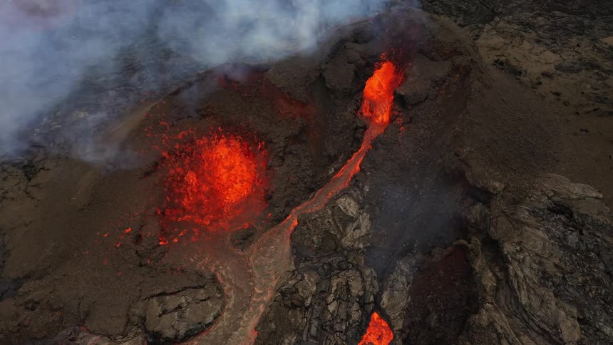 Lava pours down the slope of an erupting volcano during the day