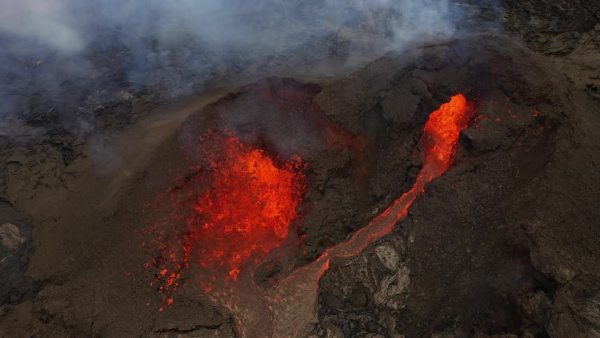 Bright red molten lava erupts from a volcano as smoke billows upwards