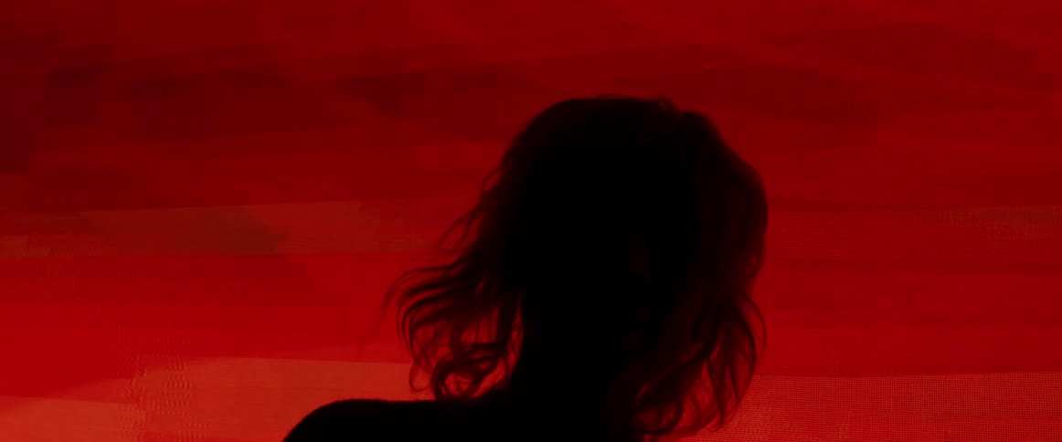 A woman dances in front of a flashing video wall in a dark room