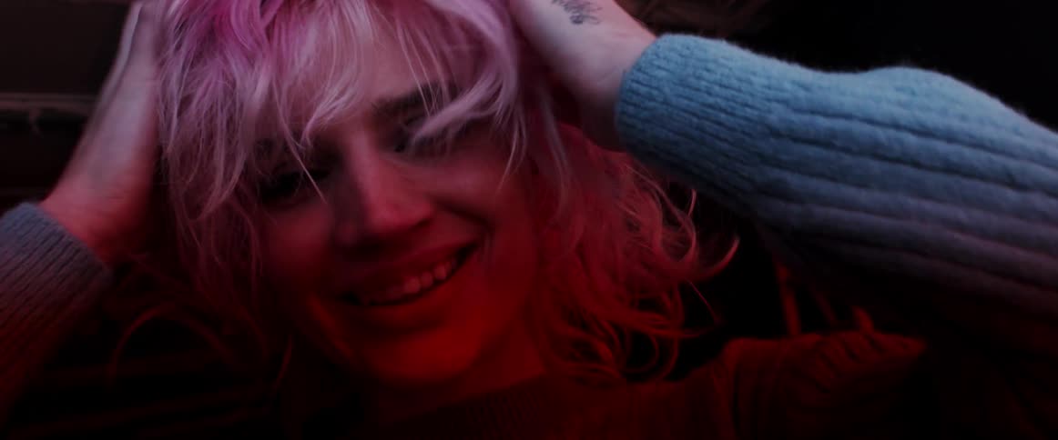 Young woman with pink hair looking at the camera on a dark room near a digital display