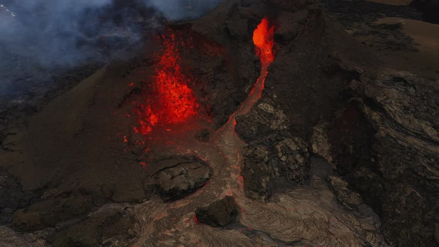 Smoke rises as an erupting volcano spews molten hot lava and oozes a river of hot lava