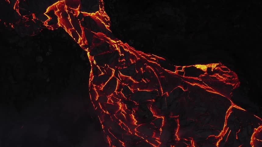 River of molten hot lava moves slowly as it glows in the darkness