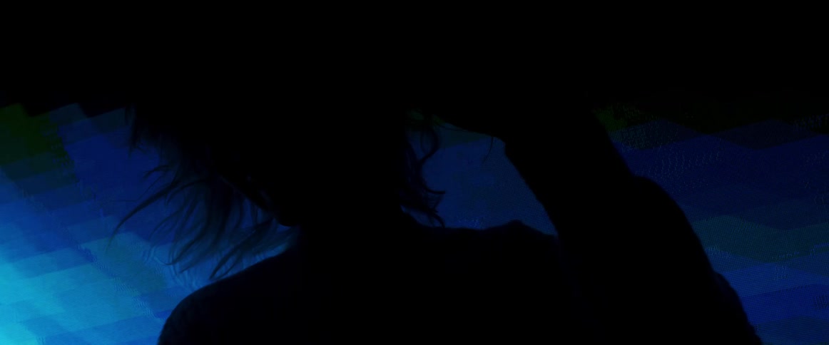 Silhouette of a young woman with pink hair dancing a on a dark room in front of a digital display