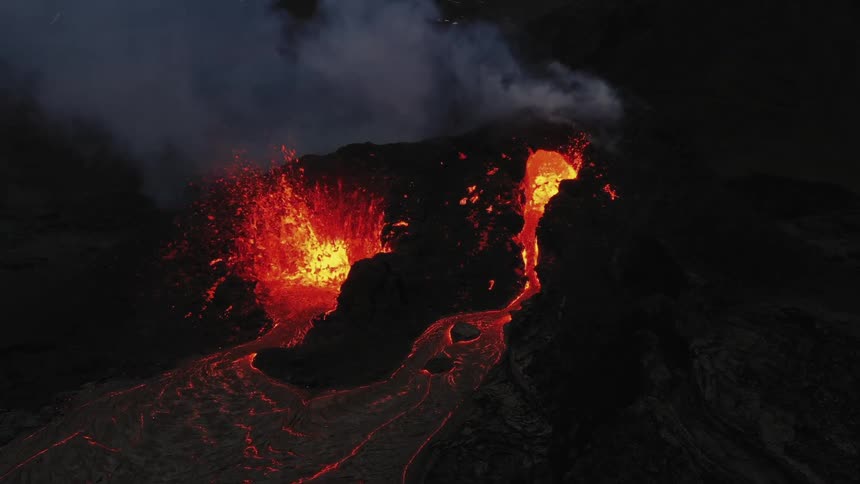 Erupting volcano spews molten hot lava into the air and oozes a river of hot lava