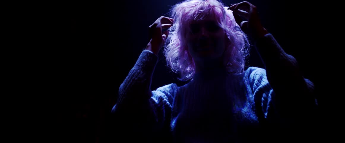 A silhouette of a woman with pink hair posing in a dark room while fluffing her hair