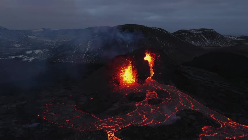 An aerial view of a volcano erupting in the evening on a mountain range