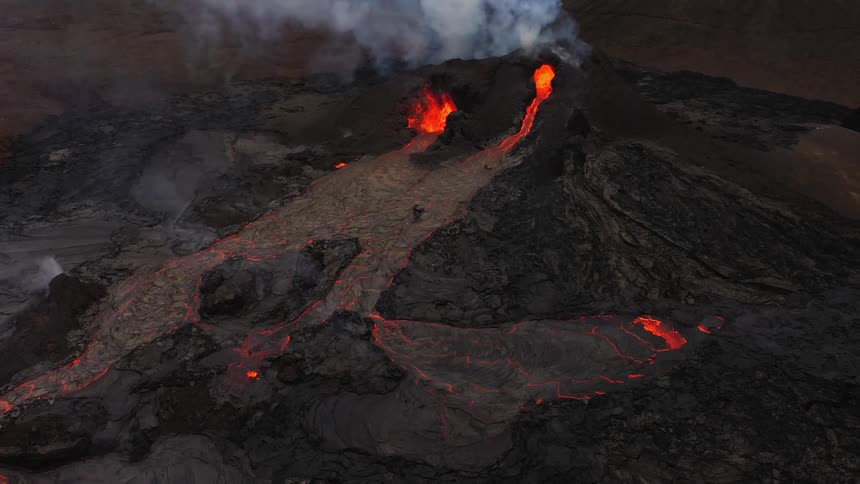 Smoke rises as an erupting volcano spews molten hot lava and oozes a river of hot lava