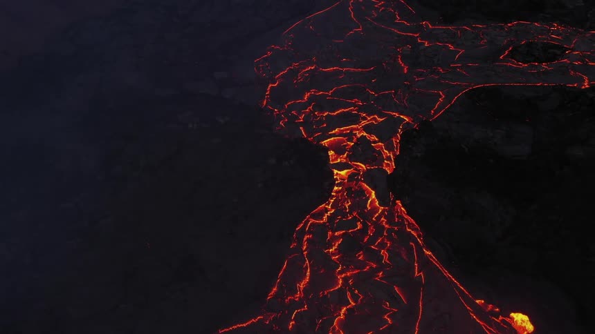 Lava flows down the side of a dark volcano as more violently erupts