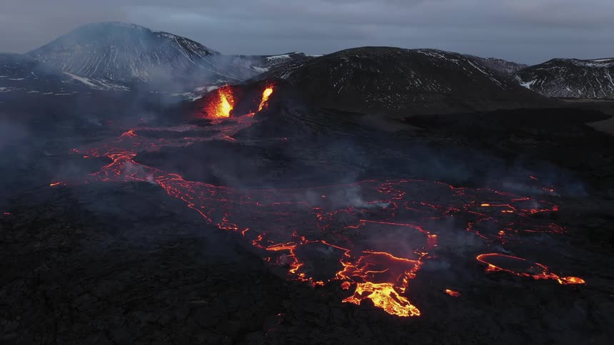 A volcano erupting with a river of molten hot lava flowing and mountains in the distance