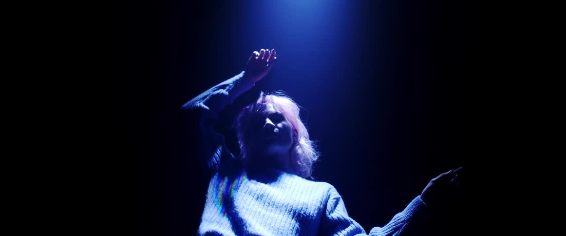 Young woman with pink hair looking at the camera on a dark room under blue lights