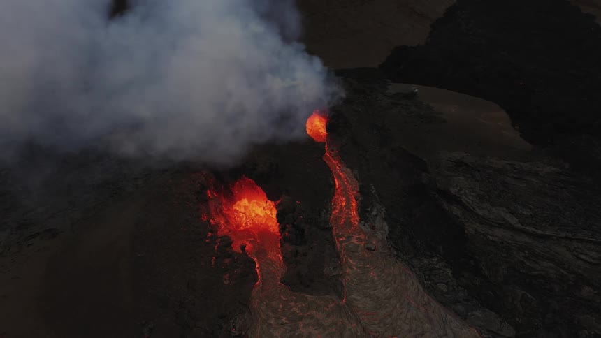 A volcanic eruption with smoke floating up into the sky on a mountain range in the evening