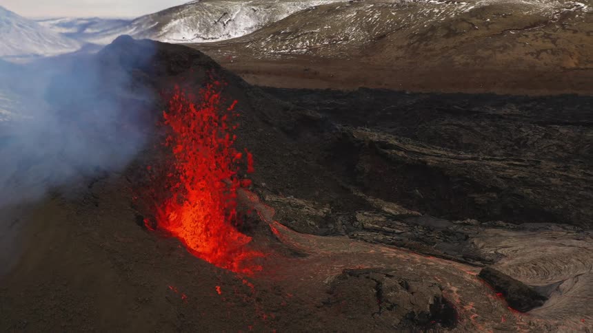 A volcano spewing molten lava with smoke with a mountain range the sky and clouds in the background