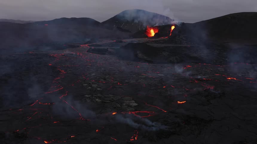 Smoke rises as an erupting volcano spews molten hot lava and oozes a river of hot lava