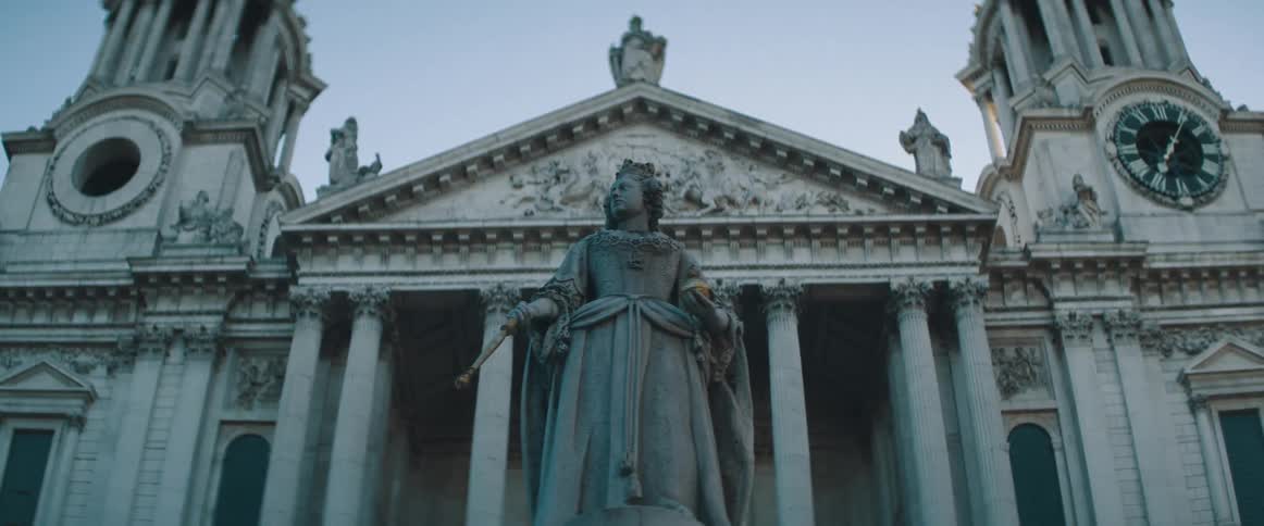 Statue of woman stands in front of ornate building with a clock in one of two towers