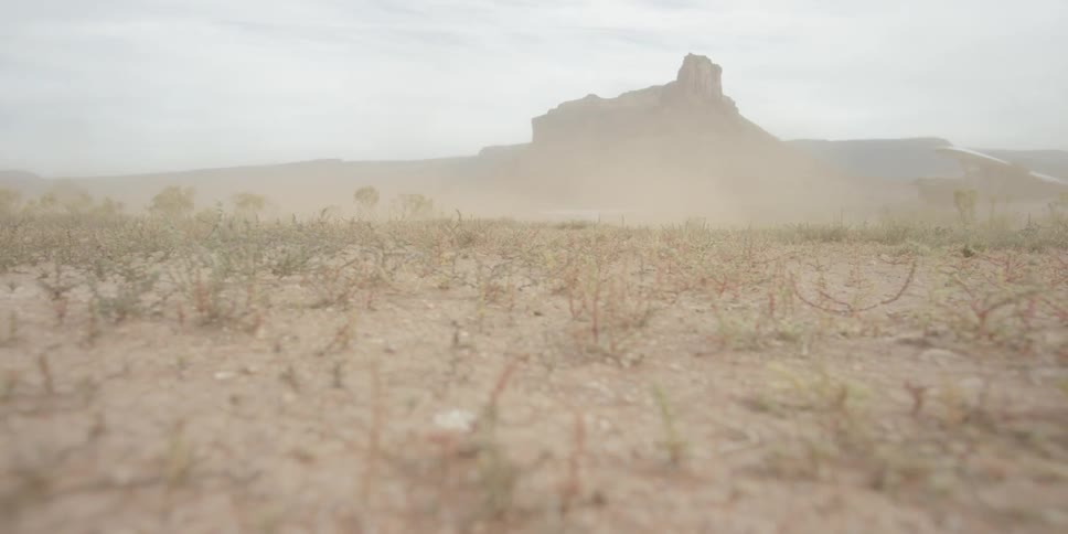 A small plane lands creating dust on a field near a large rock formation