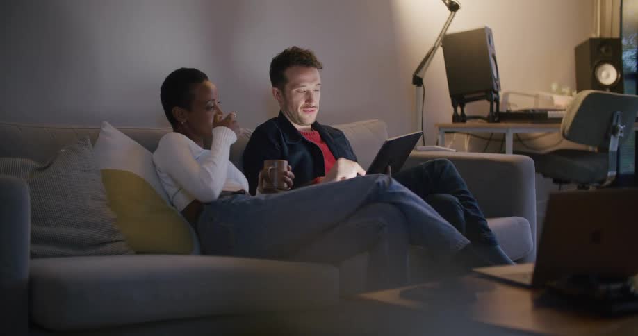A man and woman sit beside each other on a couch looking at a tablet screen