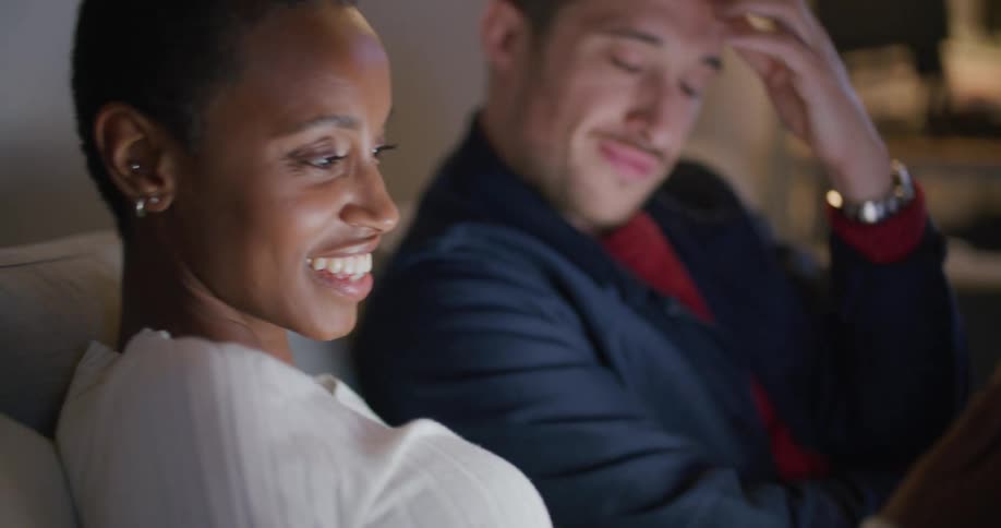 A man passes a tablet to a woman sitting beside him on a couch