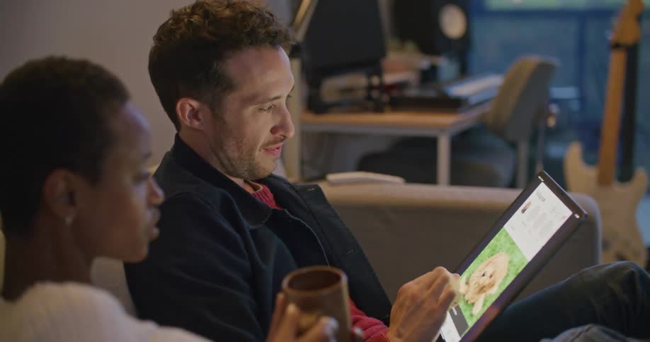 A man and woman are sitting on a couch together and looking at a tablet