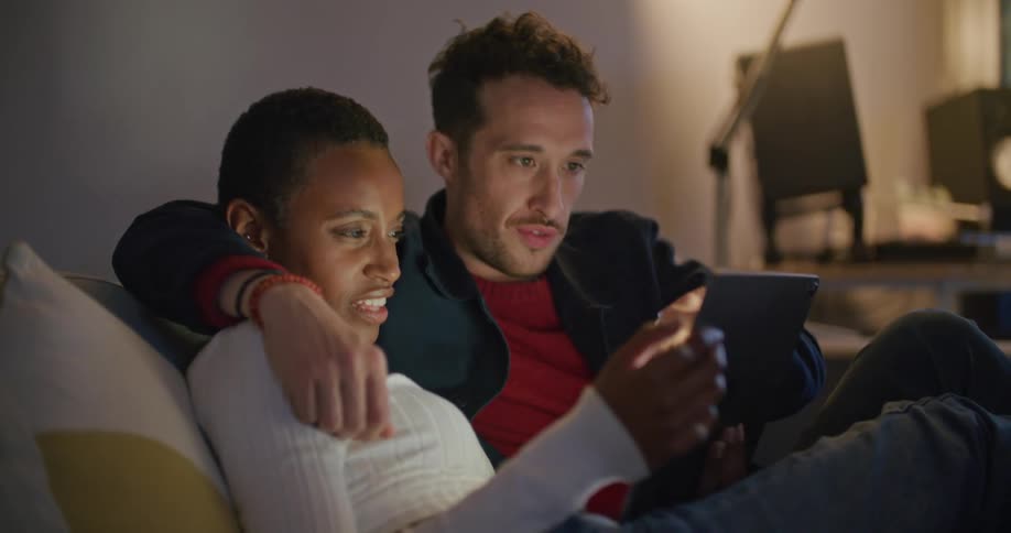 A man and woman are sitting on a couch and looking at a tablet