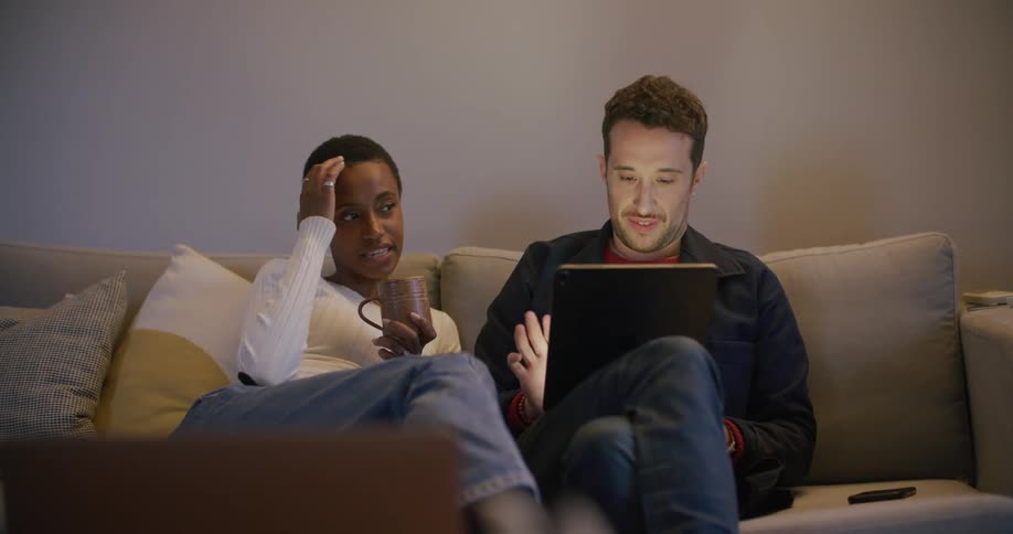 A woman talks as her husband taps away on a tablet smiling and looking at her