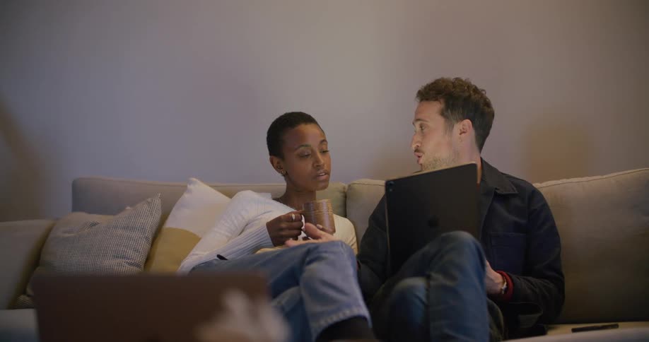 A man and a woman in a room sitting on a couch looking at a tablet