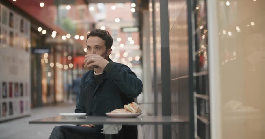 A man sitting at a table outside at a restaurant puts his phone away and starts eating a meal