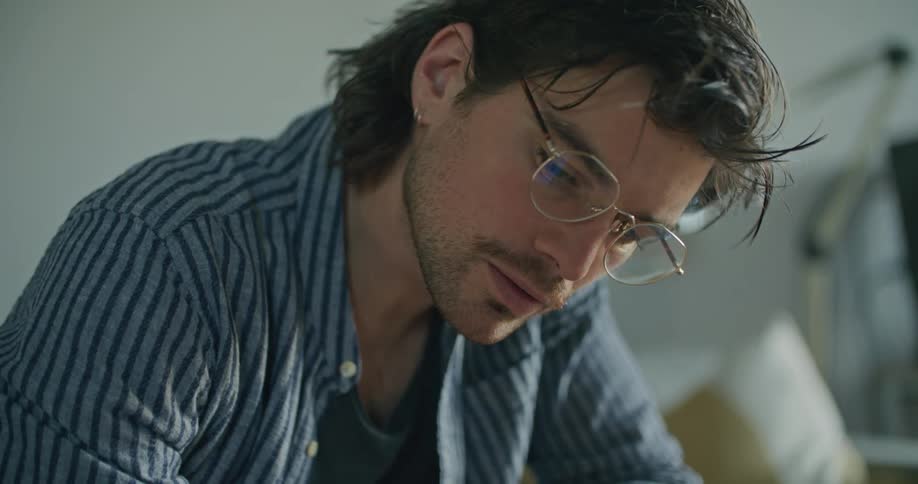 A man sits at a table writing on a piece of paper with a laptop close by