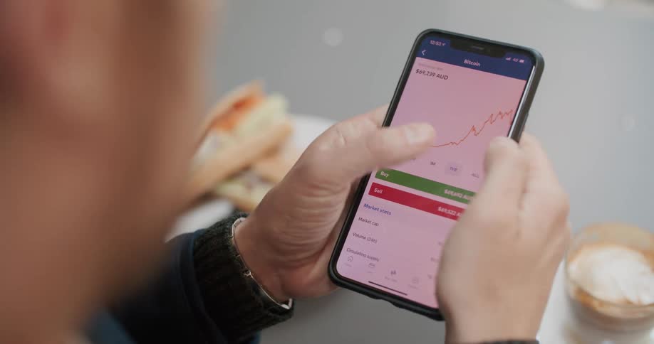 A man looking at charts on a smartphone while eating a meal
