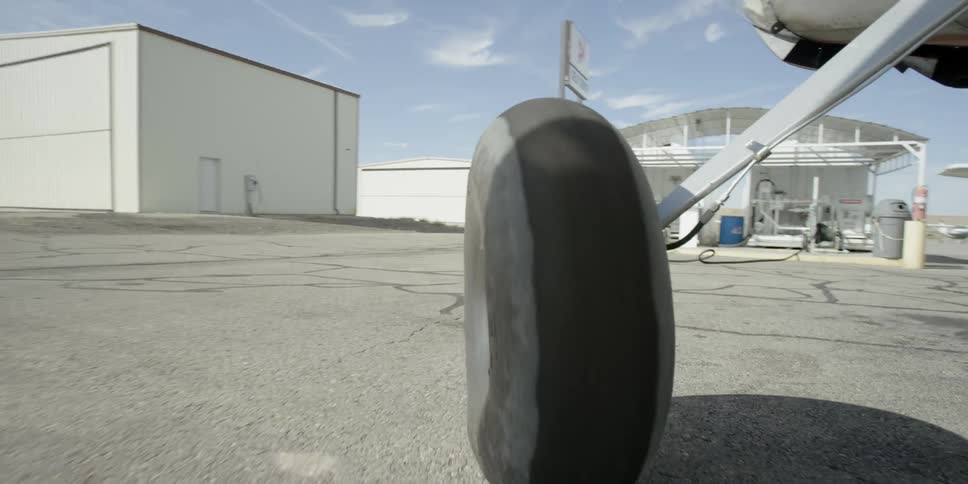 Small plane rolling on the tarmac as seen from behind one of its landing wheels
