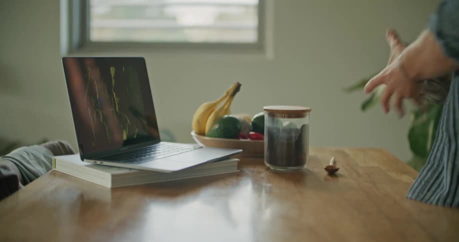 A man closes a jar before using the touchpad of a laptop on a kitchen table