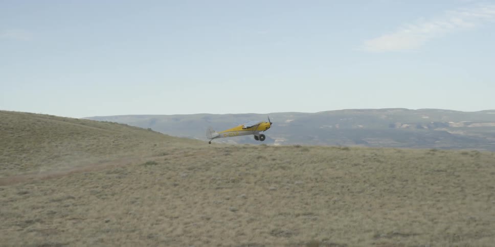 A small yellow single engine plane landing on a dirt runway in the desert