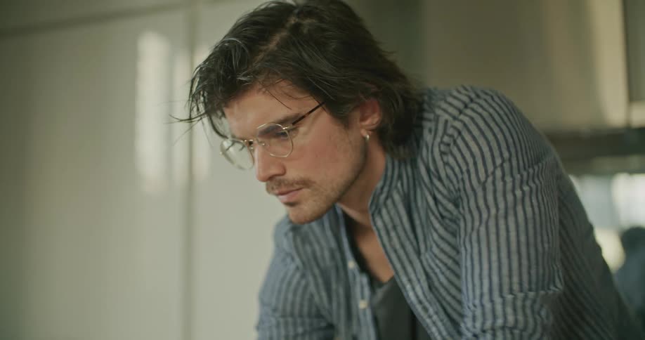 A man with glasses typing on a laptop on a table with a door in the background