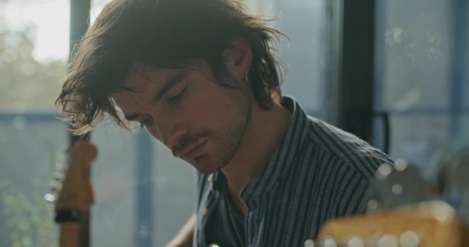 A young man focuses as he quickly plucks the strings of his bass guitar while playing it