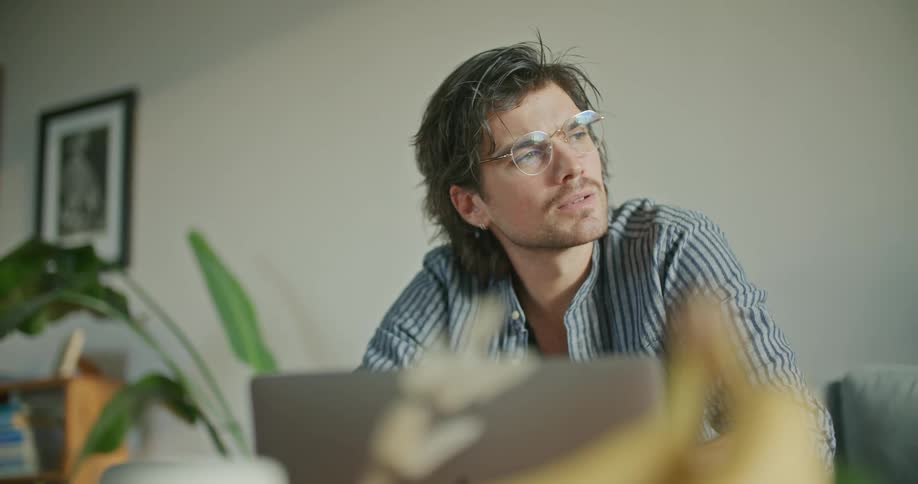 A man sits on a couch looking at a laptop with a confused expression