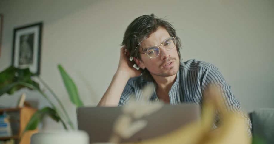 A man sits at home and scratches his head as he looks at his laptop