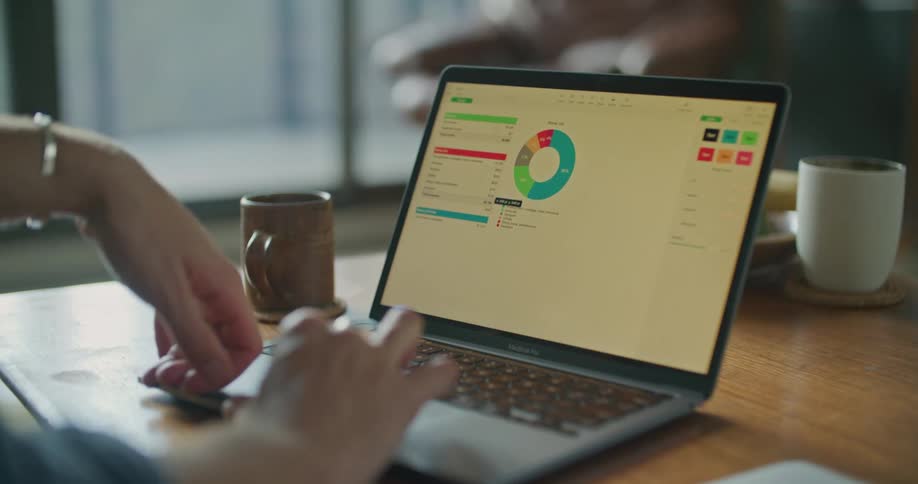 A person manipulates a graph on a laptop while sitting at a desk indoors during the day