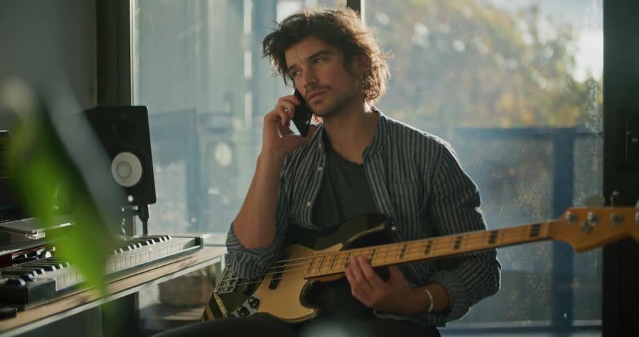 A man sits with an electric guitar talking on a cell phone