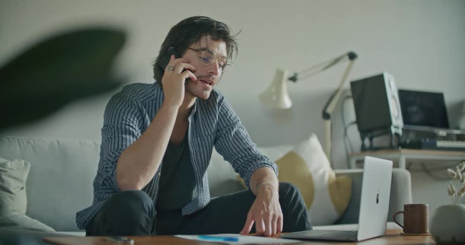 A man chats and laughs on the phone while also using his laptop