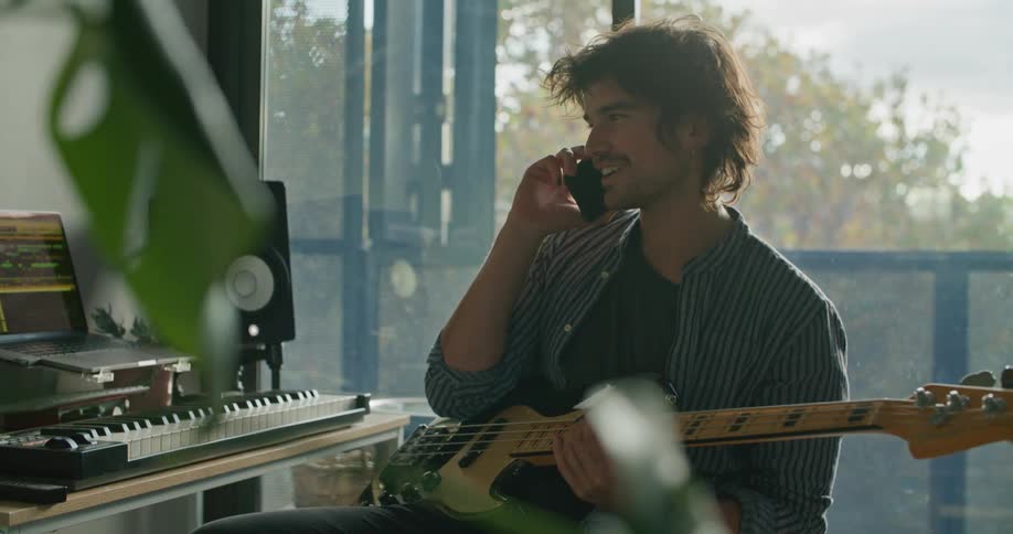 A man laughs while talking on the phone with a guitar in his lap