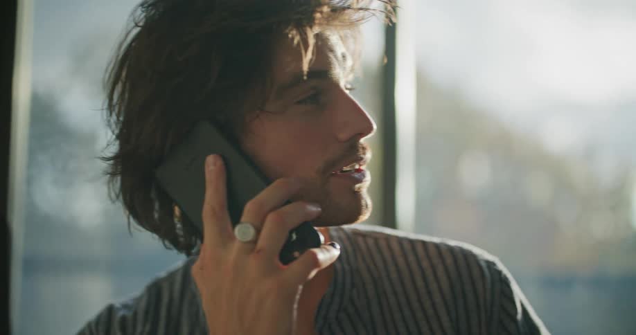 Young man holding an electric guitar talking on the phone inside a room at sunset