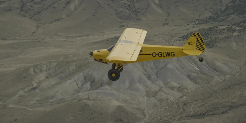 A small yellow plane flies over gulches and gullies near a mountain in the daytime