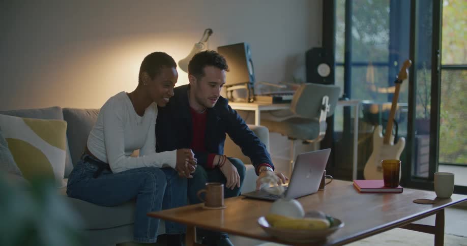 A man and woman sit on a couch and open a laptop
