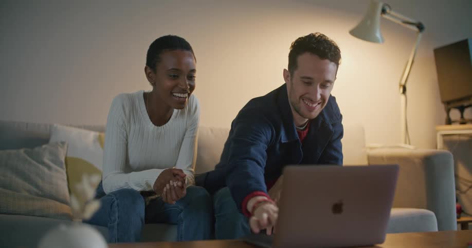 A man and woman sit at home and look at a laptop