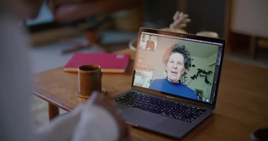 A woman on a laptop screen blows kisses at her son and daughter in law as they wave back