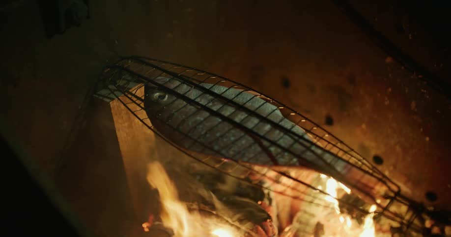 A fish in a basket being roasted on a camp fire