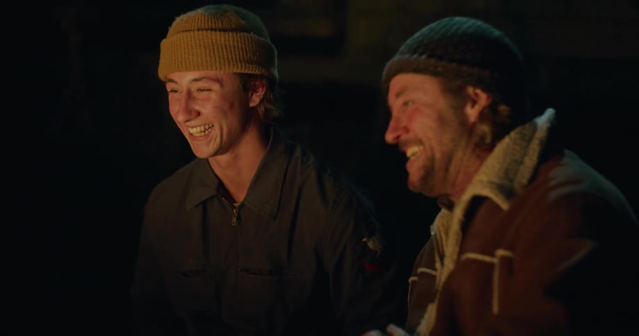 Father and son sitting outside at night in front of a flickering campfire