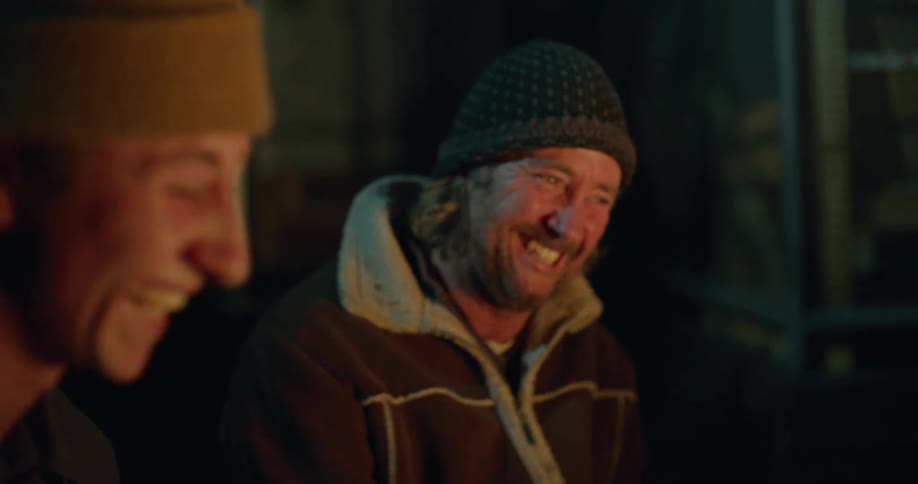 A man and his son laugh as they sit around a fire outside at night