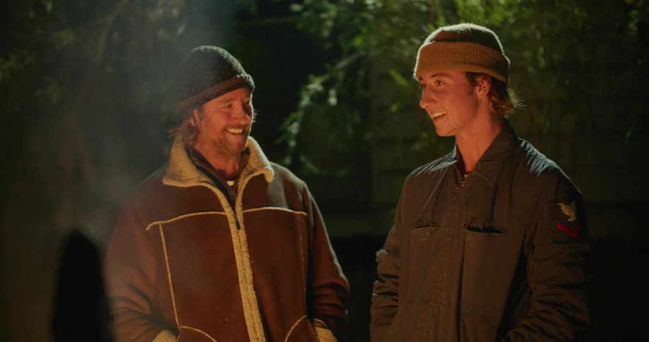 A man and teenager stand beside a campfire talking at night