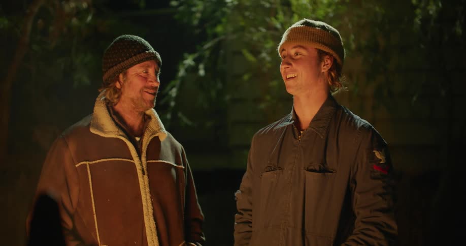 Two men standing outdoors at night time in front of a bonfire