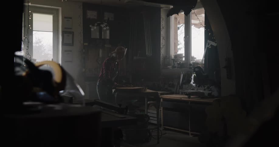 A woman places a piece of wood on top of a table in a workshop and starts working on it with a hammer